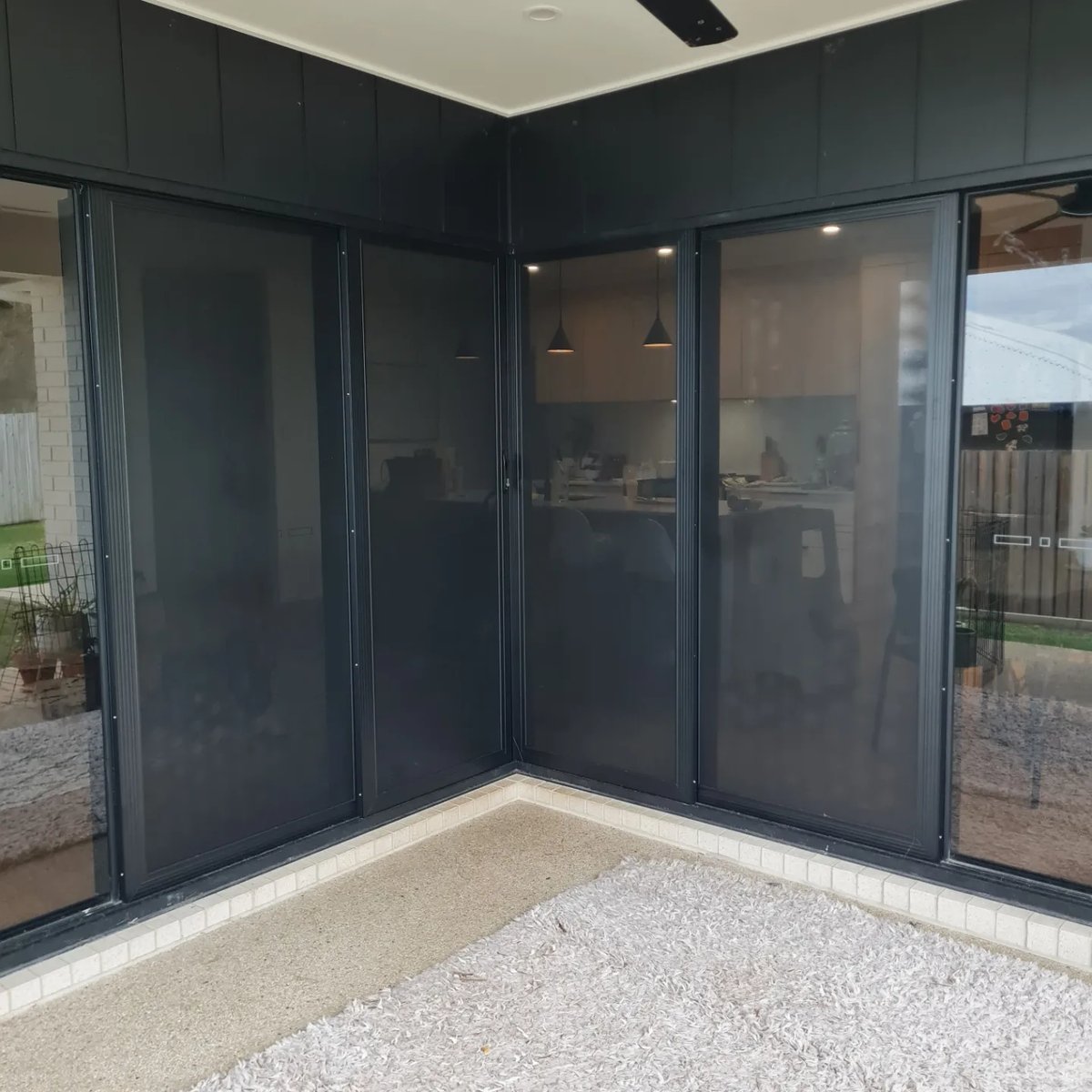 Two black framed sliding security doors meeting at the corner of a home with dark cladding